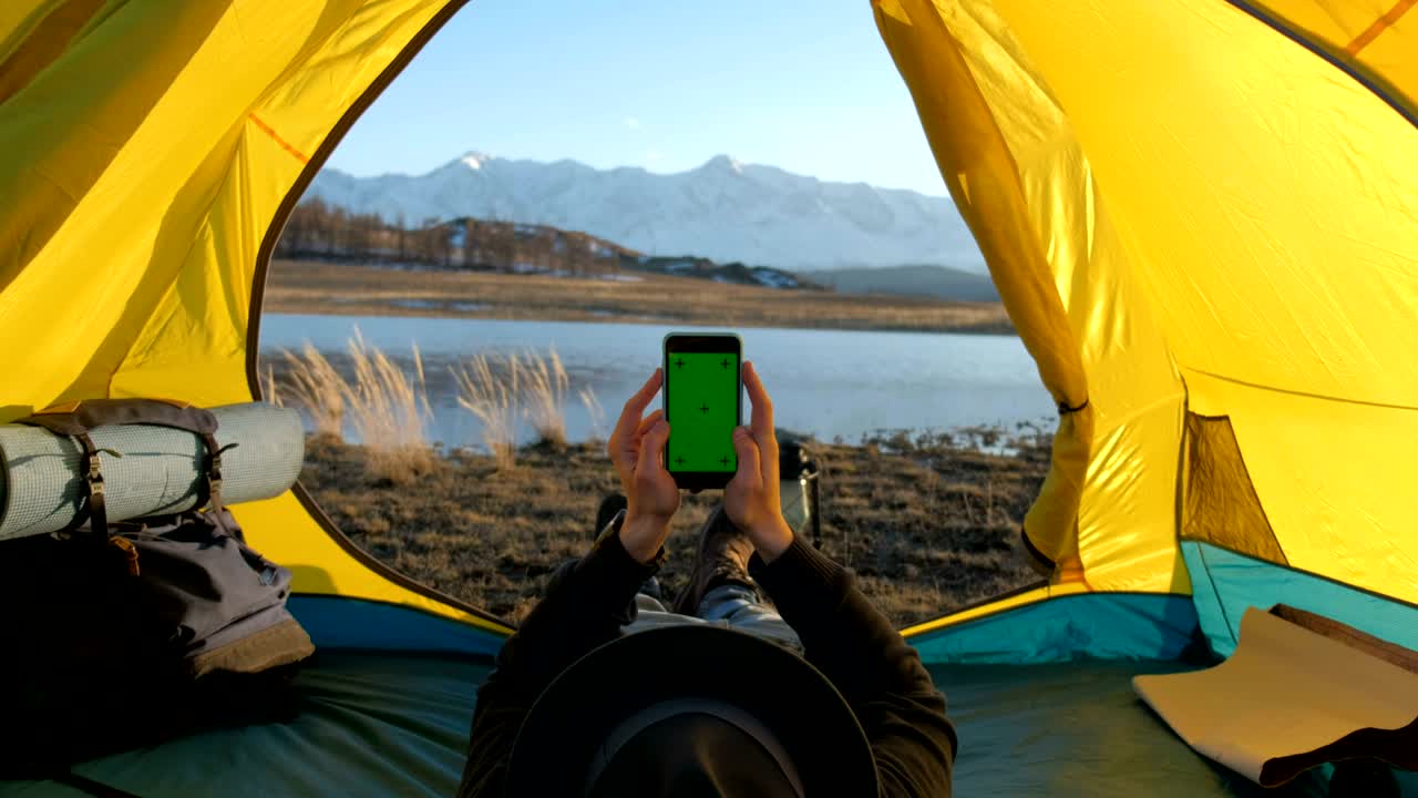텐트 에 앉아있는 남자는 태양으로부터 휴대 전화를 충전합니다.