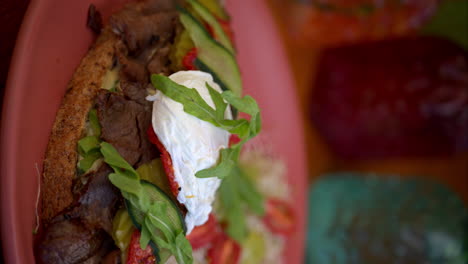 Vertical-Slow-motion-of-a-beef-deli-sandwich-topped-with-arugula-mozzarella-cheese-pickles-cucumber-and-tomato-served-with-salad