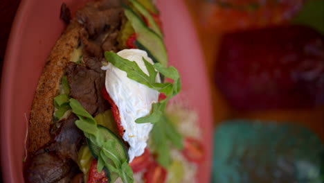 movimiento lento vertical de un sándwich de carne de res cubierto de rúcula mozzarella queso pepinillos pepino y tomate servido con ensalada