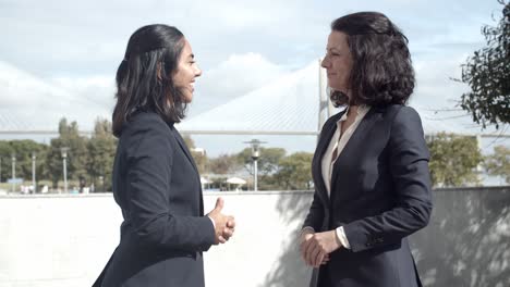 Two-pretty-businesswomen-standing-outside-and-handshaking