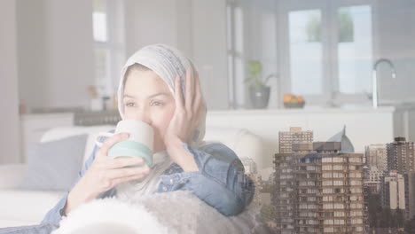 animation of cityscape over biracial woman in hijab drinking tea