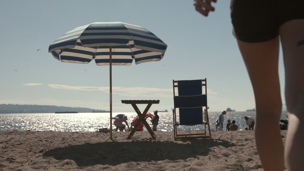 Gambe che camminano sulla sabbia della spiaggia di English Bay verso un ombrellone in una giornata di sole, Rallentatore, Vancouver.