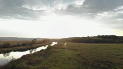 Aerial-shot-of-river-in-green-valley-at-sunset