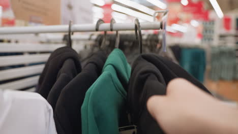 view of a shopper browsing the hoodie section in a mall and picking a black hoodie. captured with a handheld camera, this video highlights the shopping experience and detailed textures of the clothing