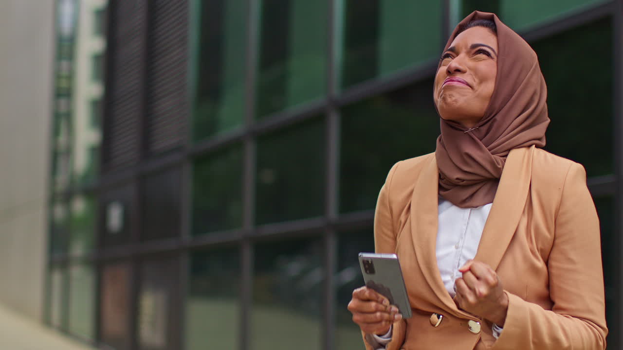 Muslim Businesswoman Wearing Hijab Standing Outside Modern Office Getting Good News About Job Offer Or Promotion On Mobile Phone 6