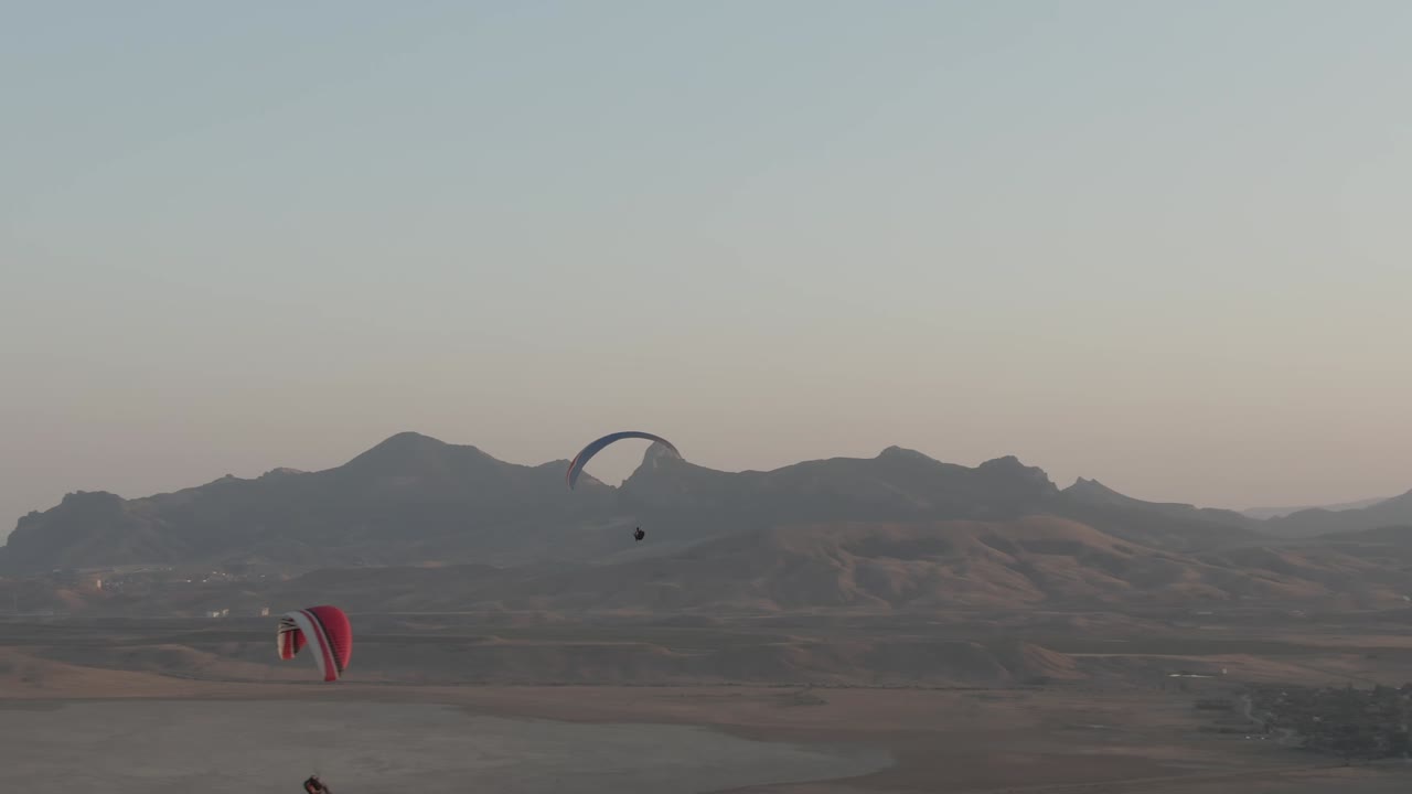 parapendio che gira sullo sfondo di una catena montuosa e di una costa marittima