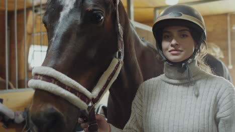 a woman stands with her horse in a stable