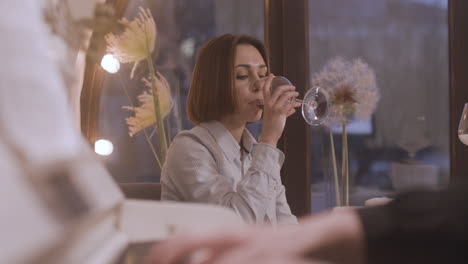 hermosa mujer sentada sola en la mesa del restaurante y bebiendo vino mientras la música femenina toca el piano