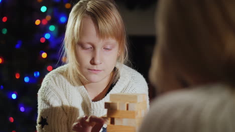 girl with mom play a board game on the background of blurry lights of festive garlands