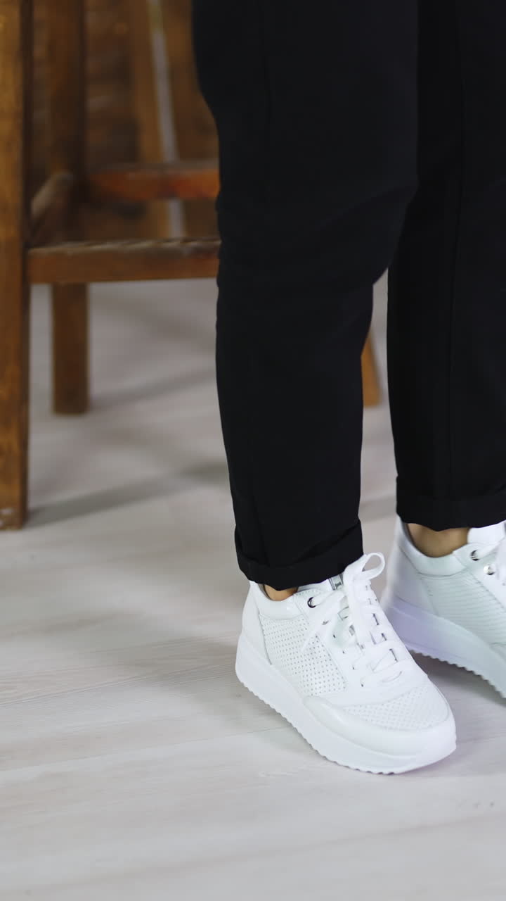 Model jumping in comfortable white sneakers. Woman spinning and hopping to demonstrate fashionable sport footwear. Vertical video