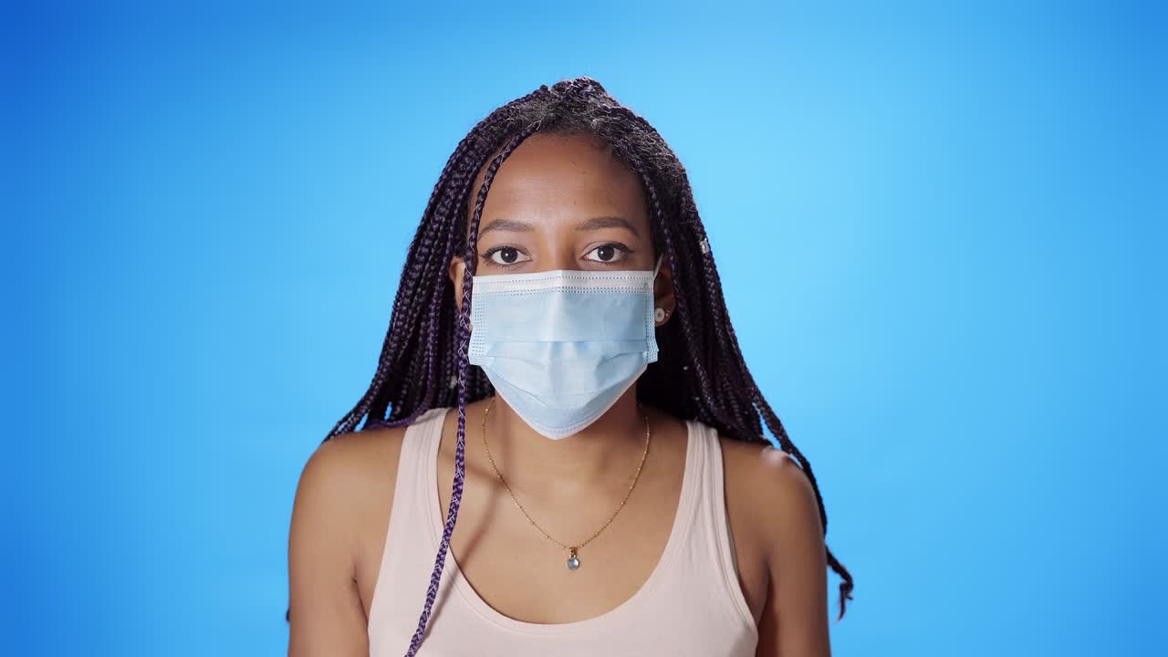Portrait of a black African American woman looking seriously at the camera putting on and taking off a mask on a blue background. Chroma key background.