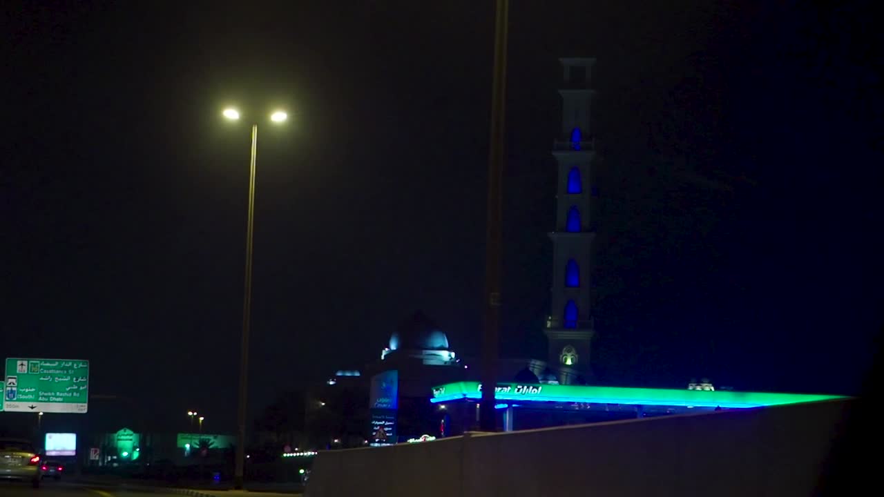 vista nocturna de una ciudad con una mezquita y una gasolinera