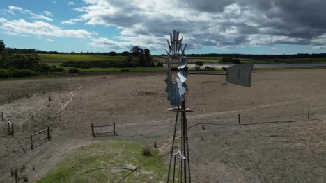 Rotierende-Rotorblätter-Einer-Windmühle-Mitten-Auf-Einem-Ackerland,-Orbitale-Dynamik-Aus-Der-Luft