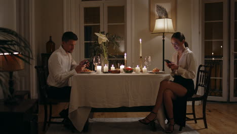 Jóvenes-Amantes-Navegando-Por-Móviles-Cena-Romántica-Cita-En-Casa.-Cónyuges-Enviando-Mensajes-De-Texto-A-Teléfonos