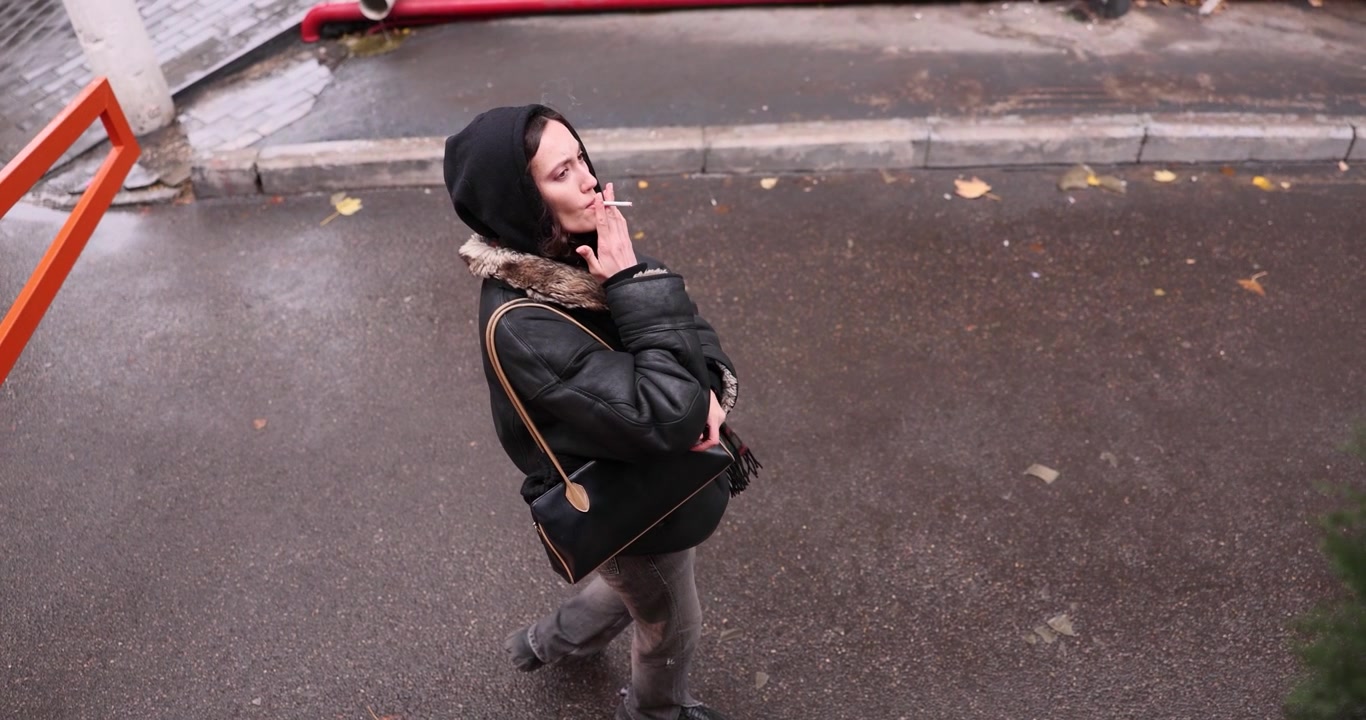 Woman lights cigarette and smokes with pensive expression outdoors