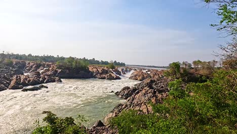a serene view of a waterfall from a wooden lookout in champasak, laos. bright daylight enhances the natural beauty and tranquility