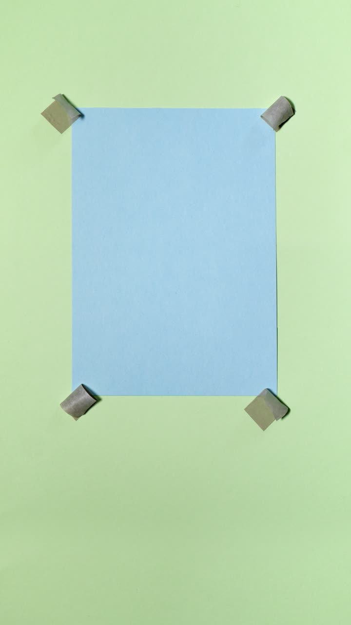 Blue paper note appears and gets taped to a pastel green background in a vertical stop motion loop with copy space