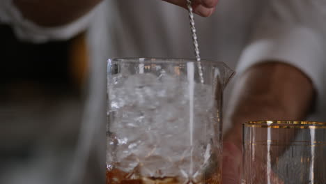 bartender stirs an old fashioned in ice in a large mixing glass