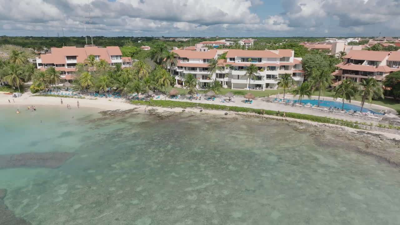 impresionante toma aérea de dolly saliendo de la playa residencial de vacaciones, revelando una hermosa playa y un mar y cielo tranquilos con nubes en un día soleado en el caribe