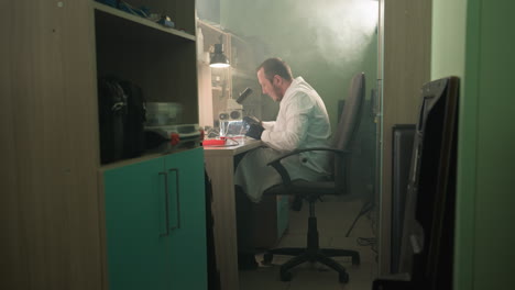 a close-up view of a technician in a white lab coat working intently under a microscope in a well-organized lab, with some tools around