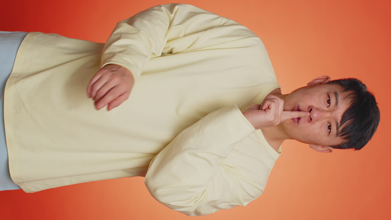 Asian man presses index finger to lips makes silence gesture sign keep my secret shh quiet please