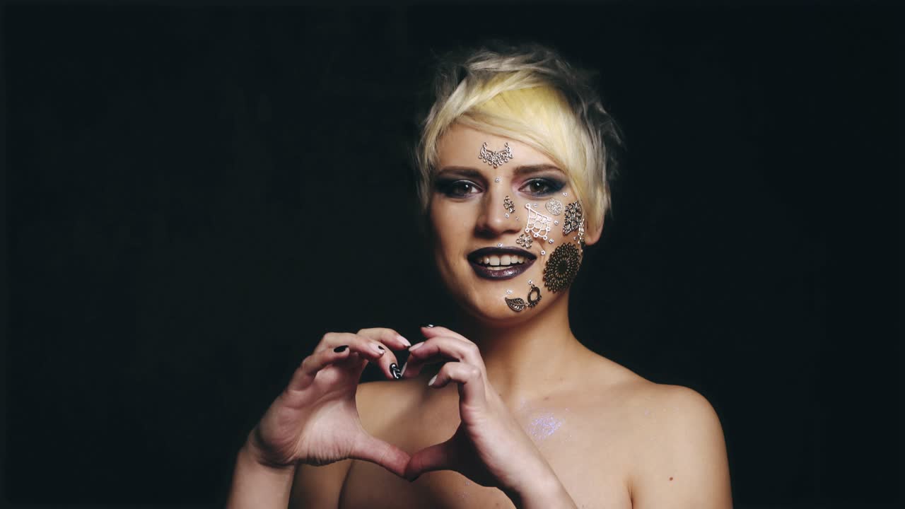 Woman showing heart shaped hands. Young attractive woman in black studio showing heart shaped hands