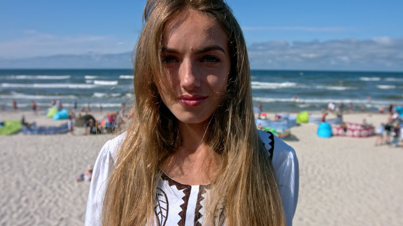 Portrait of cute woman standing on the beach full of people. Slow motion.