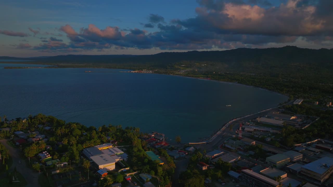 Wewak Seawall Meri beach Wewak Hill buildings cars traffic people Boram road Papua New Guinea aerial drone PNG downtown coastal town city center Dogreto Bay sunset blue sky forward down motion