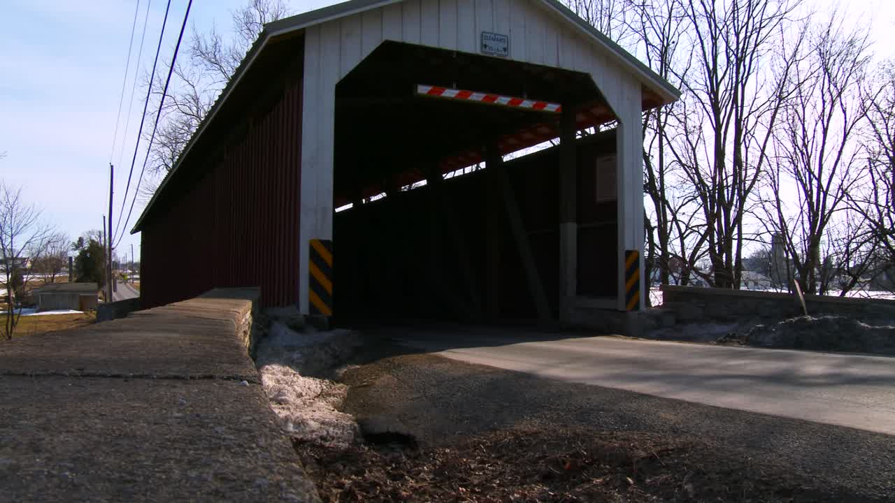 un carro de caballos amish viaja a través de un puente cubierto a lo largo de una carretera en la zona rural de pensilvania 1