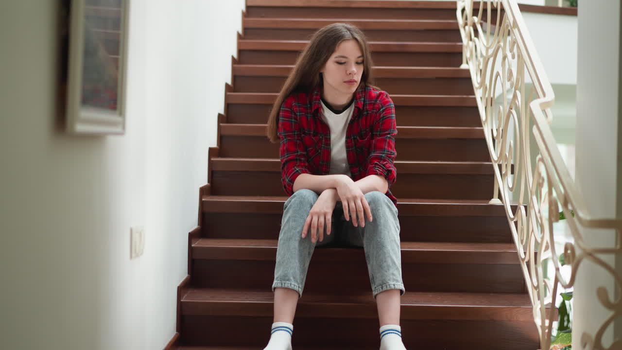 Young woman with pensive expression sits on stairs. Adult daughter sorrows about terrible quarrel with parents at home. Emotional problems overcoming