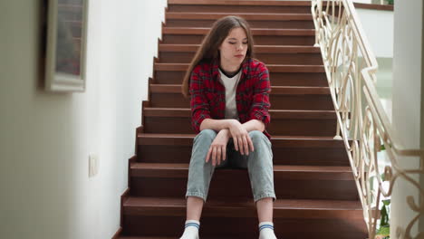 a young woman sitting on a staircase, looking down with a sad expression.