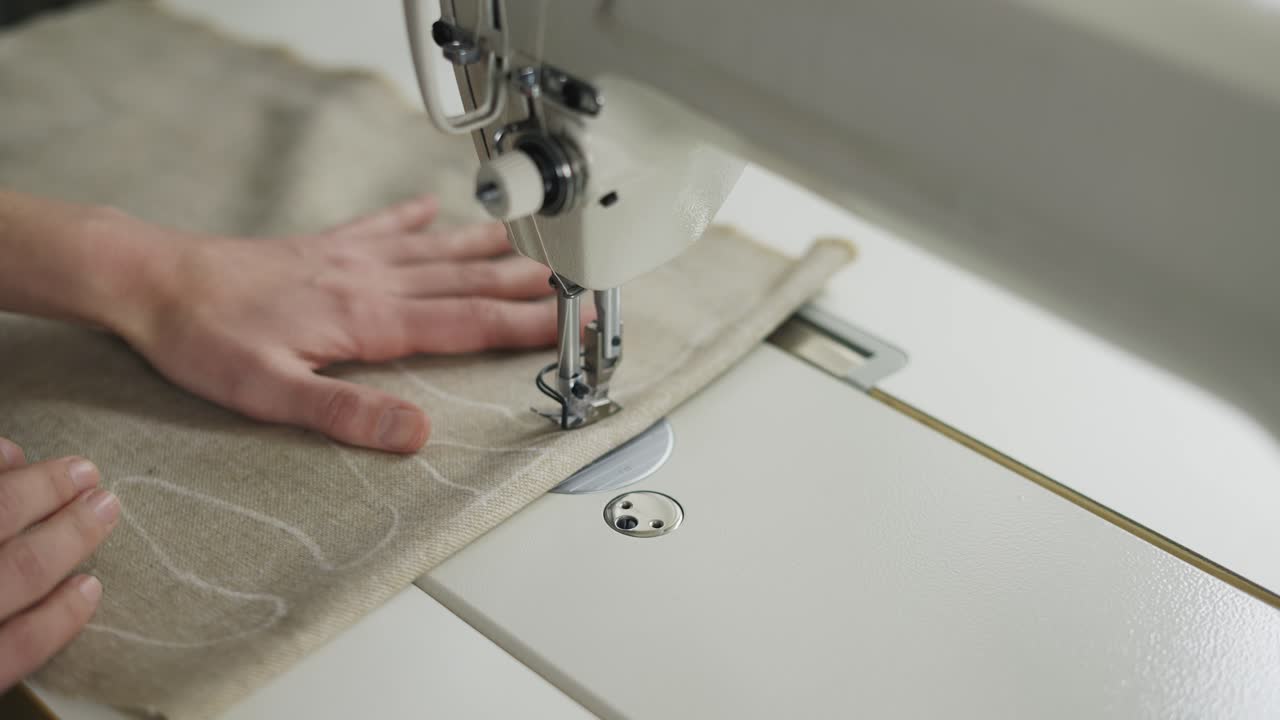 Closeup of a young woman's hands sewing beige fabric with a design