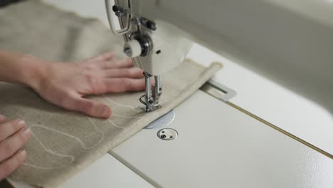 closeup of a young woman's hands sewing beige fabric with a design