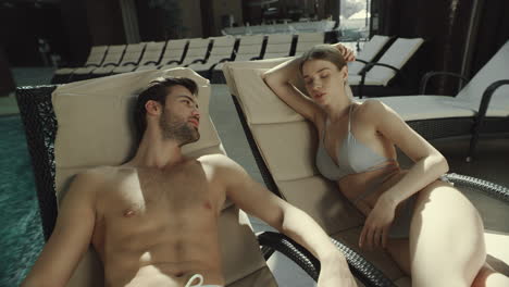 Closeup-couple-talking-on-loungers-poolside.-Man-and-woman-talking-near-pool