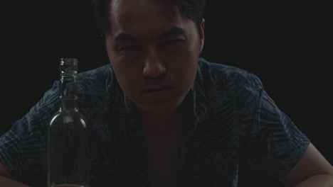 close up of drunk asian man with vodka looking at camera in black background