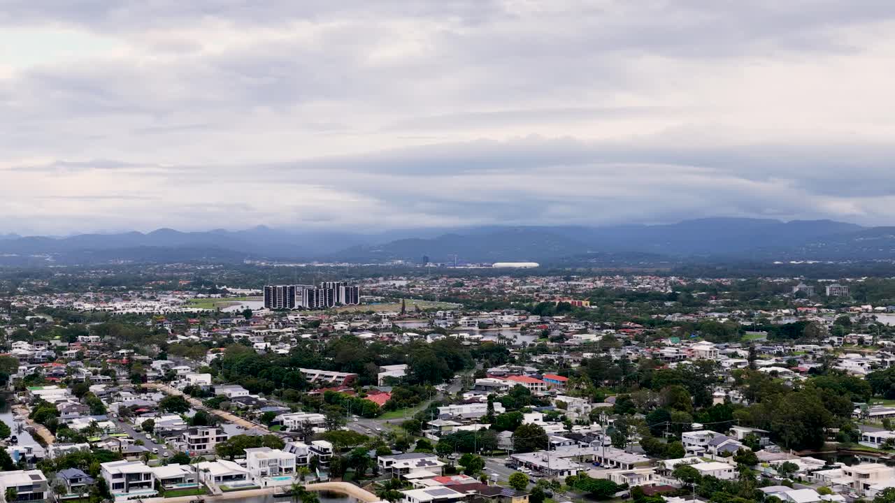 Aerial footage captures expansive cityscape with distant mountains under cloudy skies, showcasing urban and natural landscapes