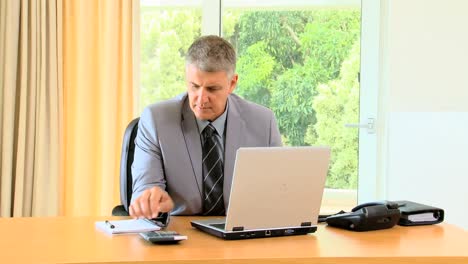 Hombre-En-La-Oficina-Trabajando-En-Una-Computadora-Portátil-Y-Usando-Una-Calculadora-De-Bolsillo