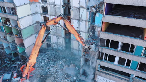 ruined building is being demolished with the help of special machinery. big claw is ruining the floors of the wrecked building. debris falling and dust raising.