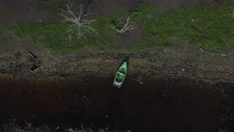 Die-Drohne-Aus-Der-Luft-Enthüllt-Ein-Fischerboot,-Das-Am-Ufer-Angedockt-Ist-Und-Von-Einem-Auffälligen-Kontrast-Aus-Blau-Und-Grün-Umgeben-Ist,-Der-Mit-Umgestürzten-Wäldern-Verflochten-Ist