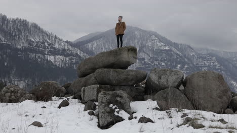 a girl stands on boulders with snowy mountains around her.