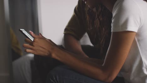 close up of young couple relaxing at home at night in bedroom looking at mobile phone together 4