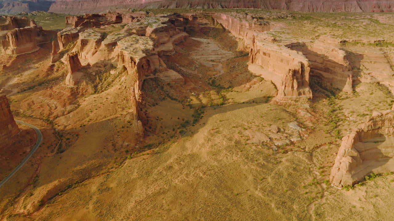 Sandy ground with scarce greenery among the huge canyons. Rocky lifeless scenery at the backdrop of blue cloudy skies. Aerial view.