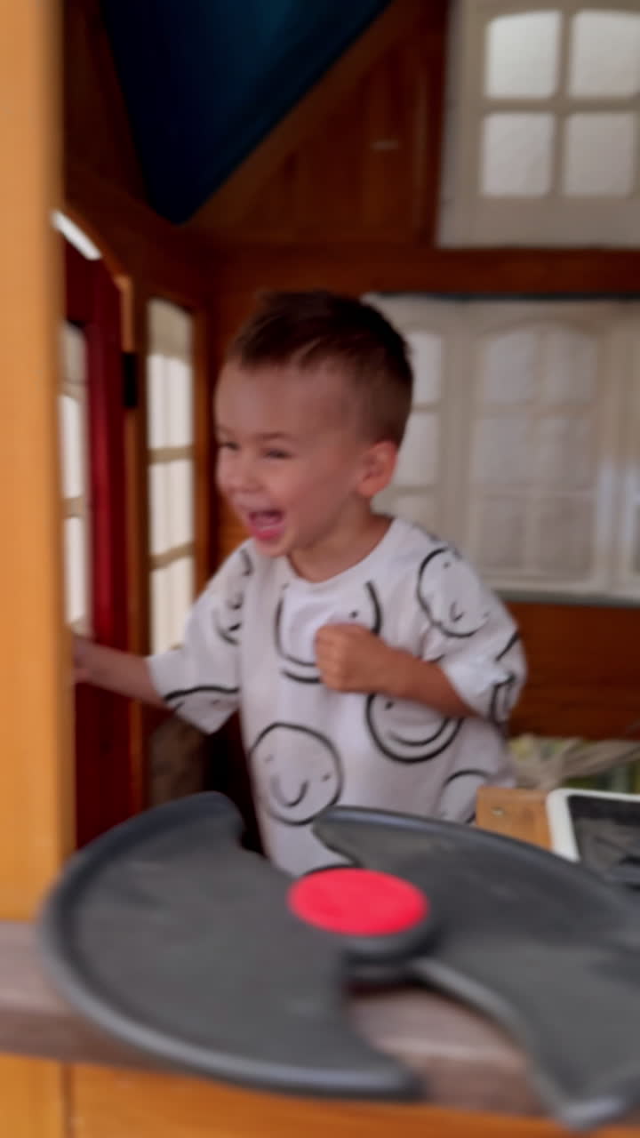 Cheerful Caucasian baby opens the doors of his playhouse and closes again. Happy kid plays hide-and-seek. Vertical video.