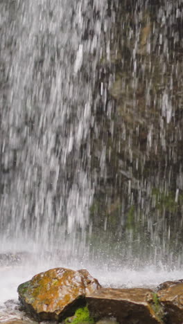 foamy waterfall jets fall down into pond with large old wet stones from high steep cliff at wild highland site on summer day slow motion