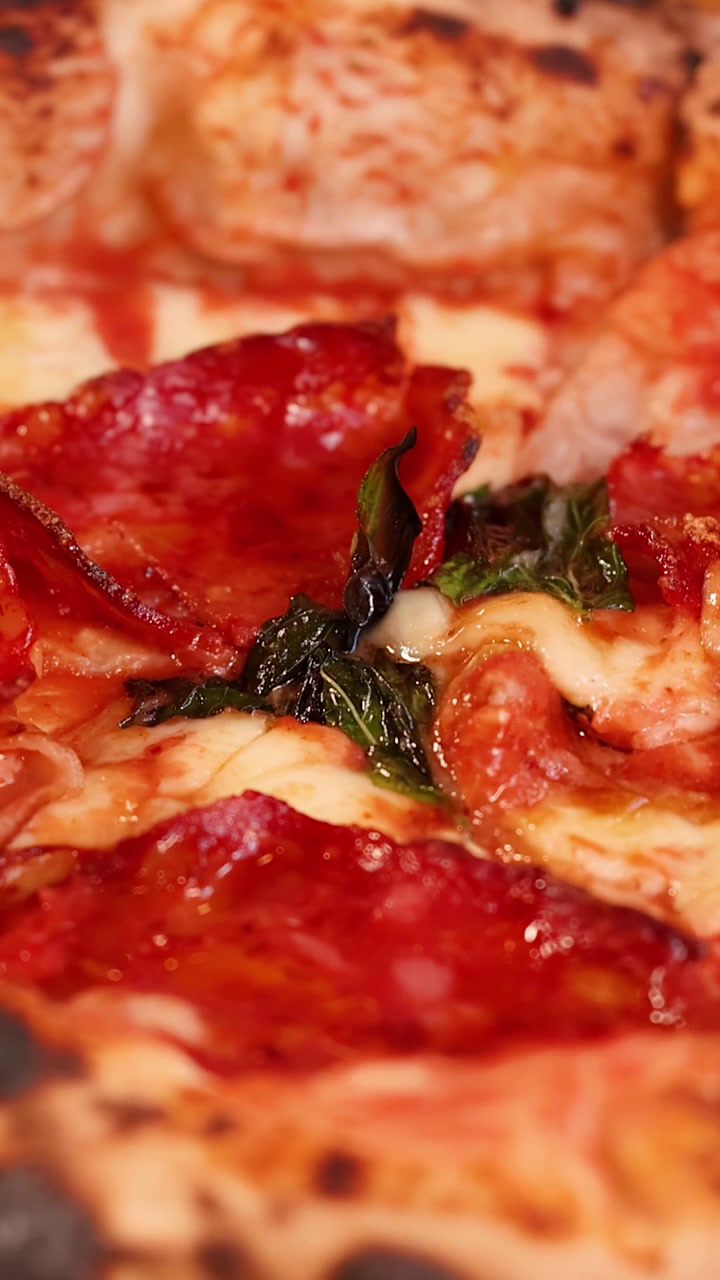 Primo piano di pizza napoletana appena sfornata con salame e basilico.