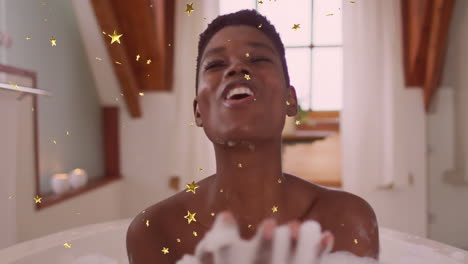 animación de estrellas doradas cayendo sobre una feliz mujer afroamericana soplando espuma en el baño
