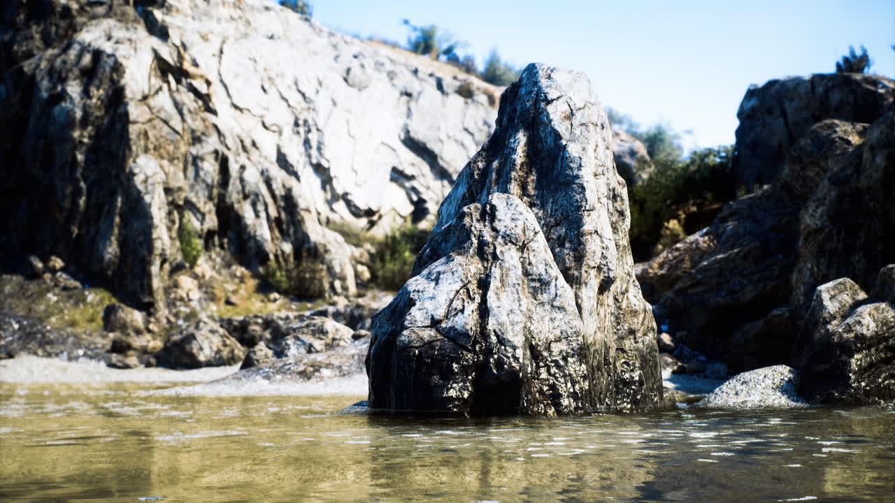 Water glistens around a large rock formation on a sunny day at the beach