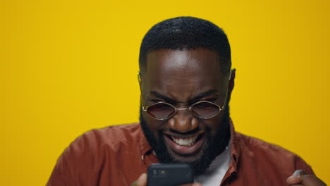 Portrait-of-excited-african-man-reading-good-news-at-smartphone-in-studio.