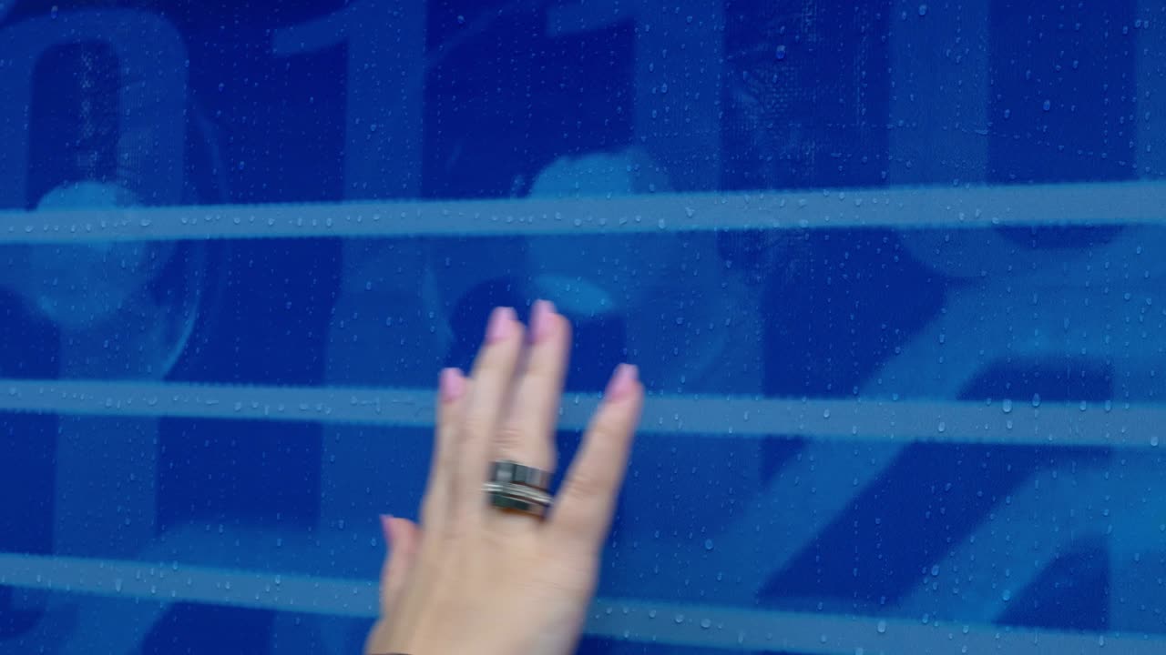 한 여자의 손은 파란 발에서 흘러내리는 비방울을 그리며, 손가락으로 물방울을 그림의 줄을 따라 그리며, 그녀의 손가락에는 은 반지가 있습니다.