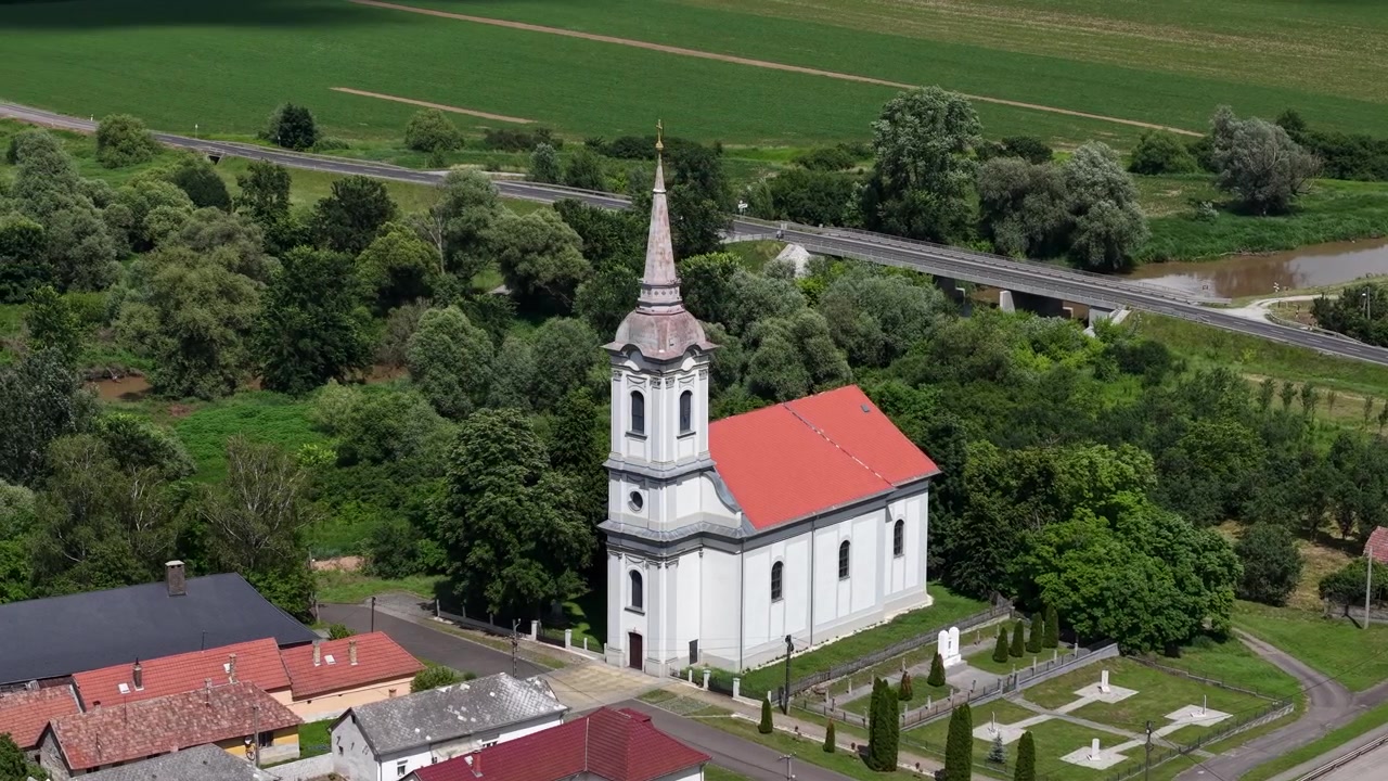 Et luftfoto av en hvit kirke med rødt tak i en ungarsk landsby, omgitt av trær og jorder